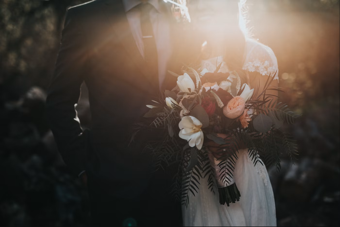 An outdoor wedding ceremony setup with white chairs, a floral arch and soft natural light at golden hour